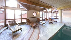 Un área de piscina interior con tumbonas de madera y suelo de baldosas.