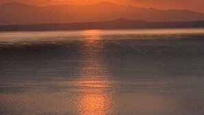 Auringonlasku tyynen vesistön yllä, taustalla vuoria.
