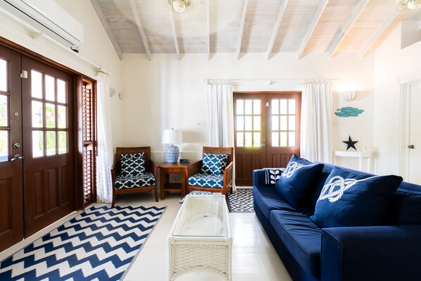 Ein Wohnzimmer mit einem blauen Sofa, gemusterten Sesseln, einem Glastisch und einem chevron-gemusterten Teppich.