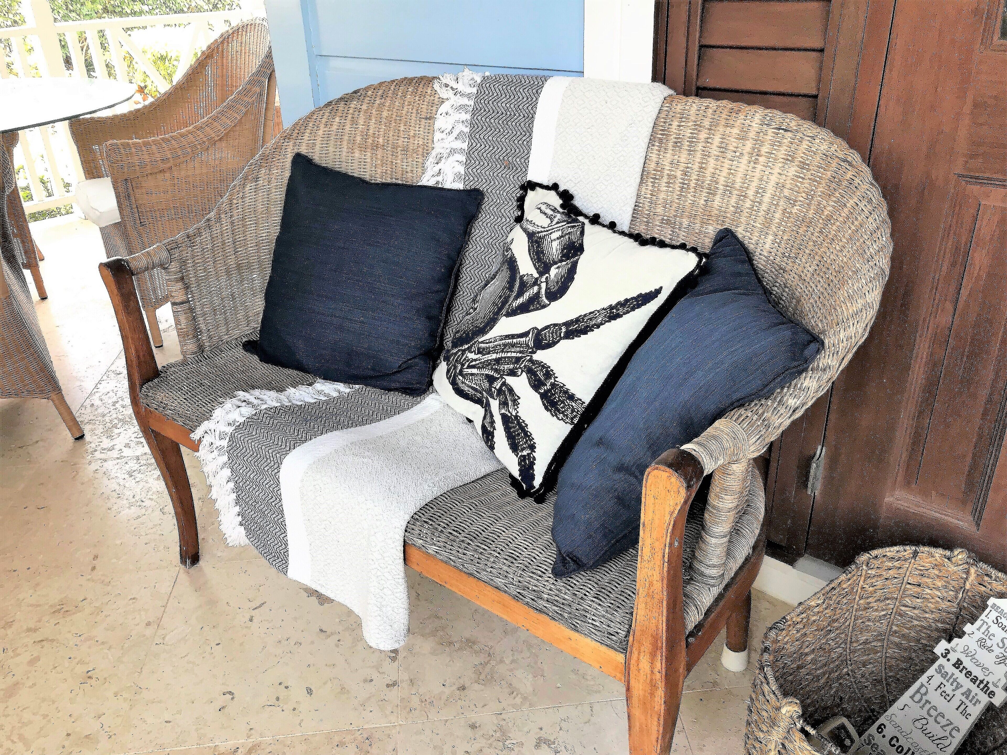 A wicker chair with a white and black patterned throw blanket, two pillows, and a wooden floor.