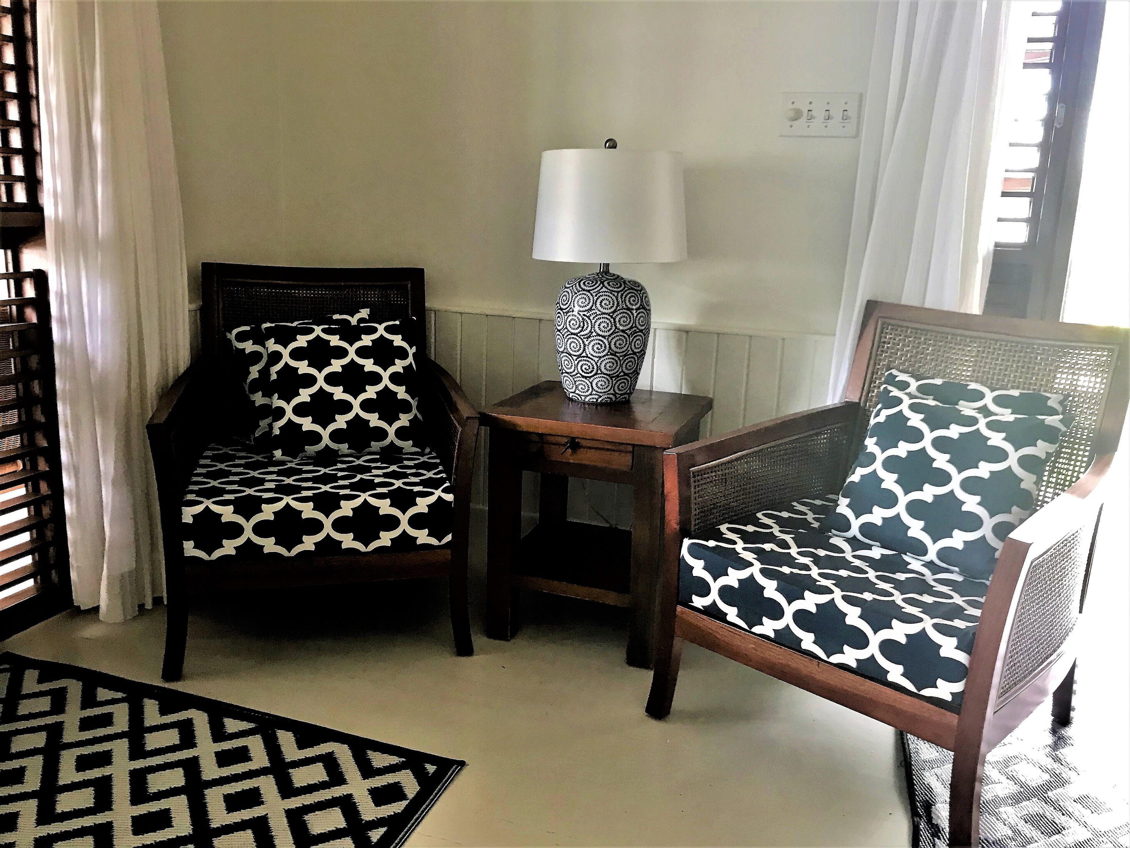 A room with two patterned chairs, a small table with a lamp, and a geometric rug.