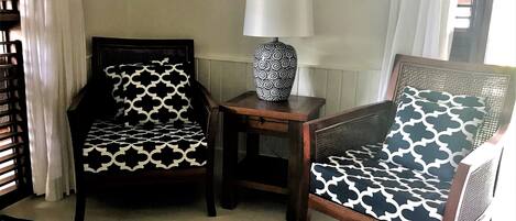 A room with two patterned chairs, a small table with a lamp, and a geometric rug.