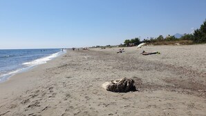Une plage avec un grand rocher au premier plan, quelques personnes au loin et un ciel dégagé.