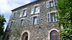Un bâtiment en pierre doté de nombreuses fenêtres et de volets, avec des portes en arc de cercle et une apparence rustique.