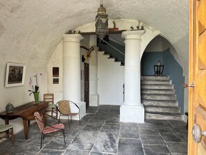 Een interieur met stenen vloer, een wenteltrap, een houten deur en een eethoek met stoelen en een tafel.