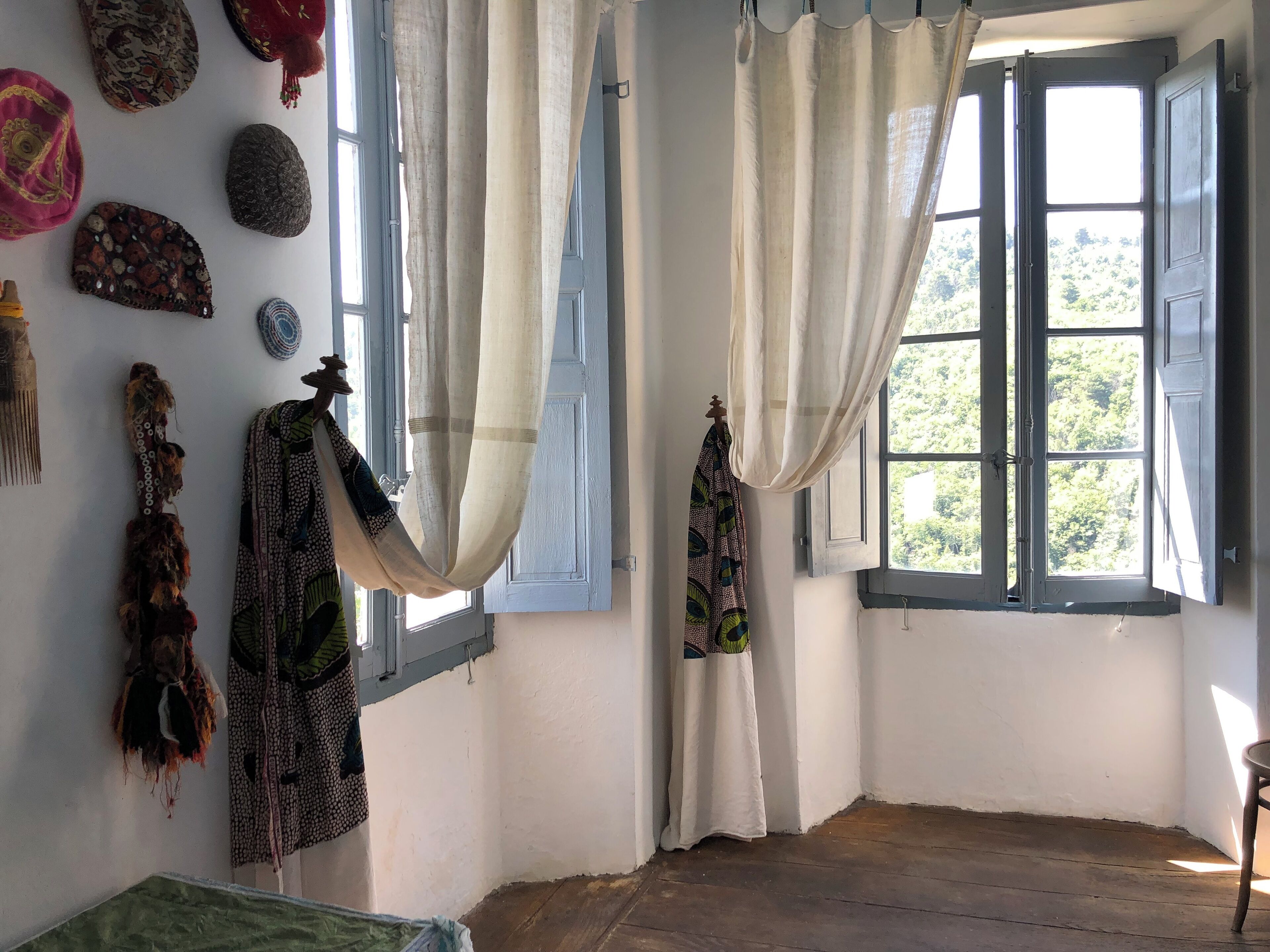 A room with a wooden floor, a window with white curtains, and various decorative items on the wall.