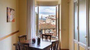 A dining area with a table and chairs, a view of buildings through an open door, and a painting on the wall. - A Fantabulous Dreaming Terrace in FLORENCE Ponte Vecchio (Firenze)