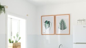 Une cuisine moderne avec des meubles blancs, un plan de travail en bois, un four encastré et un évier. Deux reproductions botaniques encadrées ornent le mur, et une fenêtre offre une vue sur un cactus.