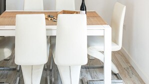 Un coin repas avec une table blanche, des chaises blanches, un filet suspendu avec un tissu blanc et un appareil de climatisation fixé au mur.