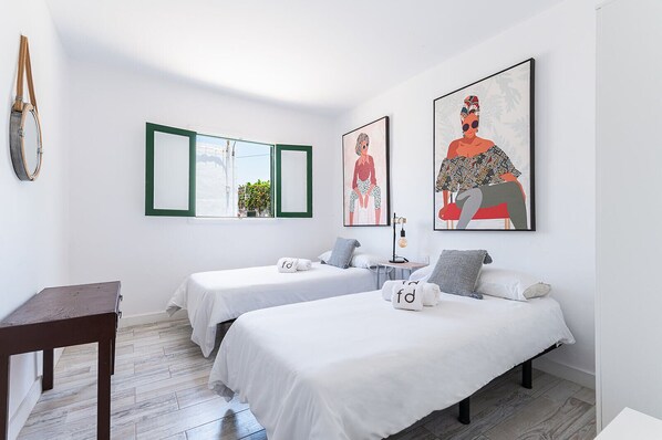 A modern hotel room with two single beds, a small table, and artwork on the walls.
