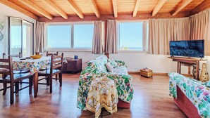 A cozy room with wooden beams, a dining table with chairs, a sofa, a TV, and large windows with curtains. - Villa with exclusive swimming pool 5 minutes from the sea (Palermo)