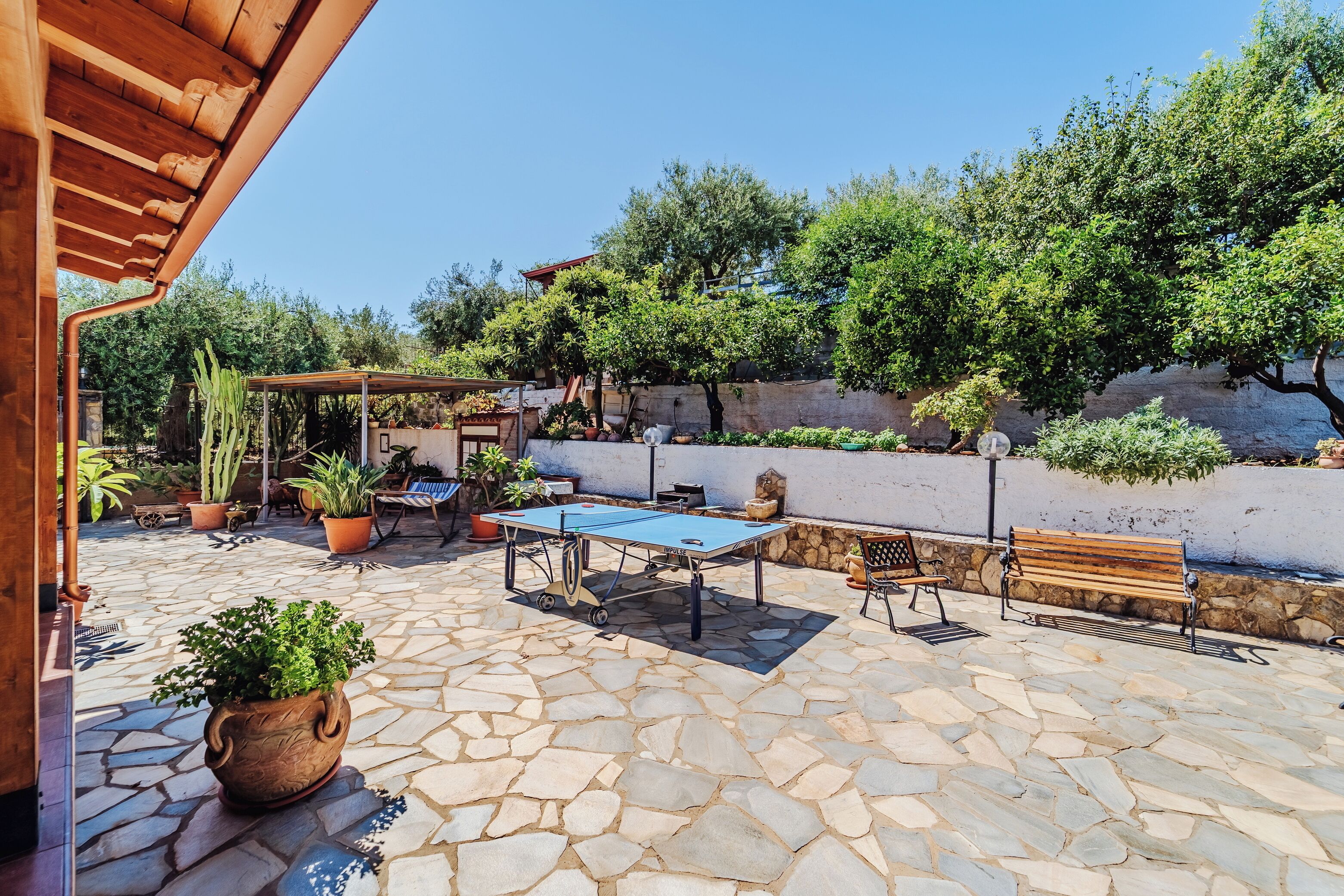Une terrasse extérieure avec un sol en pierre, une table de ping-pong et divers plantes en pot.