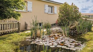 Een rustige tuin met een vijver, een houten hek en een gebouw met luiken.