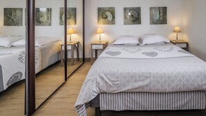 Een slaapkamer met een grote spiegel, twee nachtkastjes met lampen, een bed met een gestreept dekbed en wanddecoratie met schelpen.