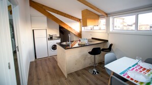 A modern kitchen with wooden beams, a built-in washing machine, and a dining area with a table and bar stools.