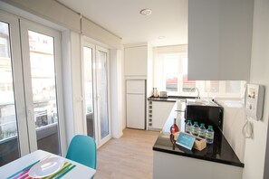 A modern kitchen with a refrigerator, microwave, and toaster. There is a dining area with a table and chairs, and a balcony with a view of the city. - Camões 691 Design Apartments by Porto City Hosts (Porto)