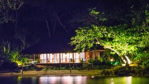 A waterfront property with a wooden deck overlooking a calm body of water, surrounded by lush greenery.