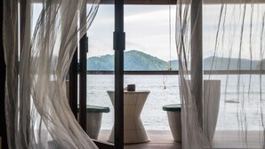A room with a view of the sea, a wicker table, and a hanging light fixture.