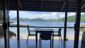 A wooden deck with a table and chairs overlooking a calm sea and green hills.