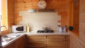 Une petite cuisine aux murs en bois, équipée d’un four à micro-ondes, d’une cuisinière et d’une horloge murale.