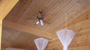 Une chambre avec deux lits, des murs en bois, un ventilateur de plafond et une armoire blanche.