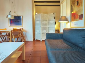 A room with a dining table, chairs, a sofa, a lamp, a wall art piece, and a wicker partition. - Penthouse in the heart of Barcelona. Rambla E (Barcelona)