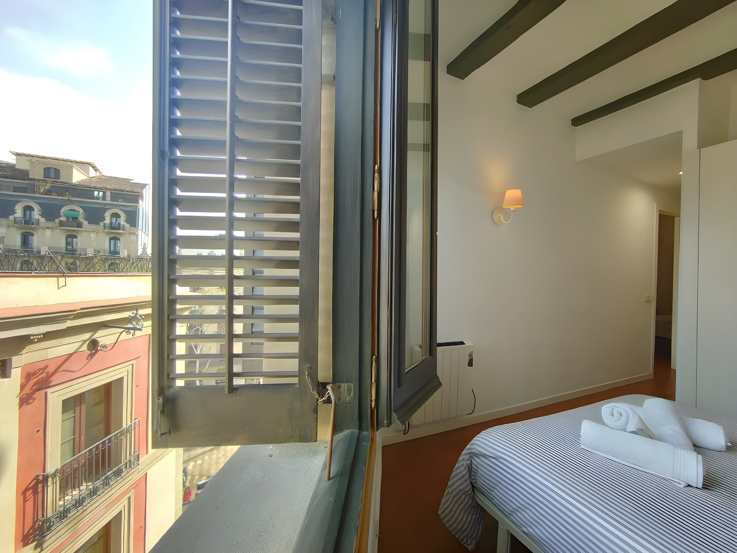A balcony with metal railings, a bed with a striped bedspread, and a white wall with a light fixture.