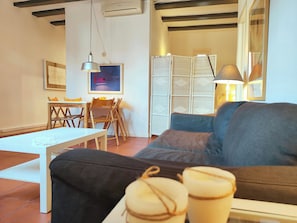A living room with a sofa, a dining table with chairs, a hanging lamp, and a bookshelf.