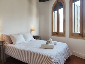 A bed with striped bedding, a bedside lamp, and a window with shutters.