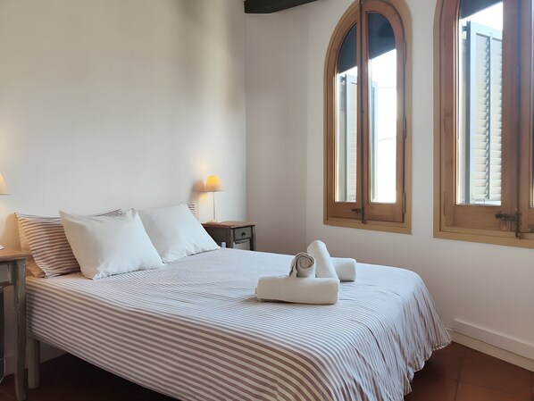A bed with striped bedding, a bedside lamp, and a window with shutters.