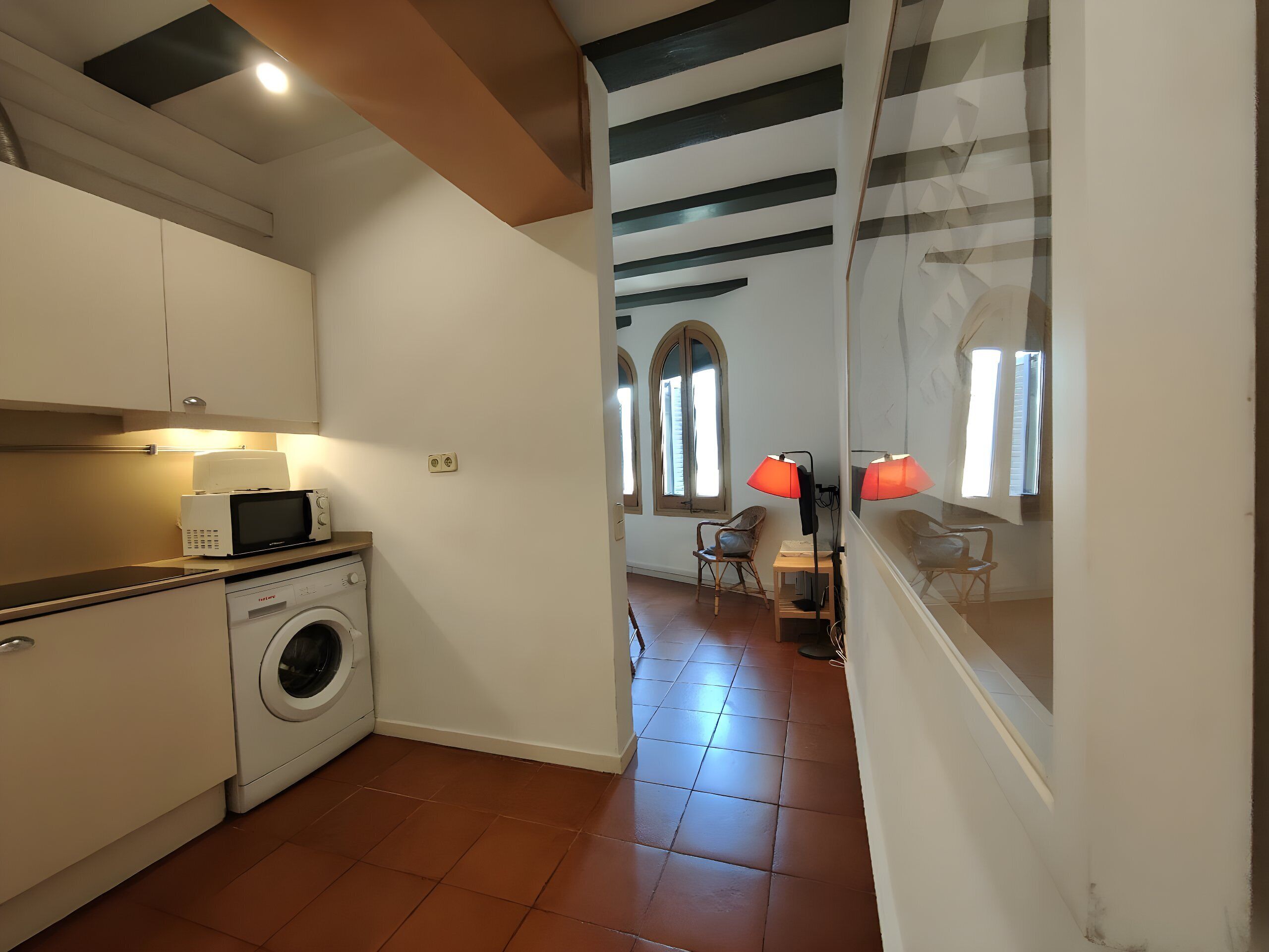 Une cuisine compacte équipée d’un lave-linge, d’un four à micro-ondes et d’une petite table avec des chaises.