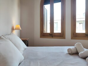 A hotel room with a bed, a lamp, and two windows.