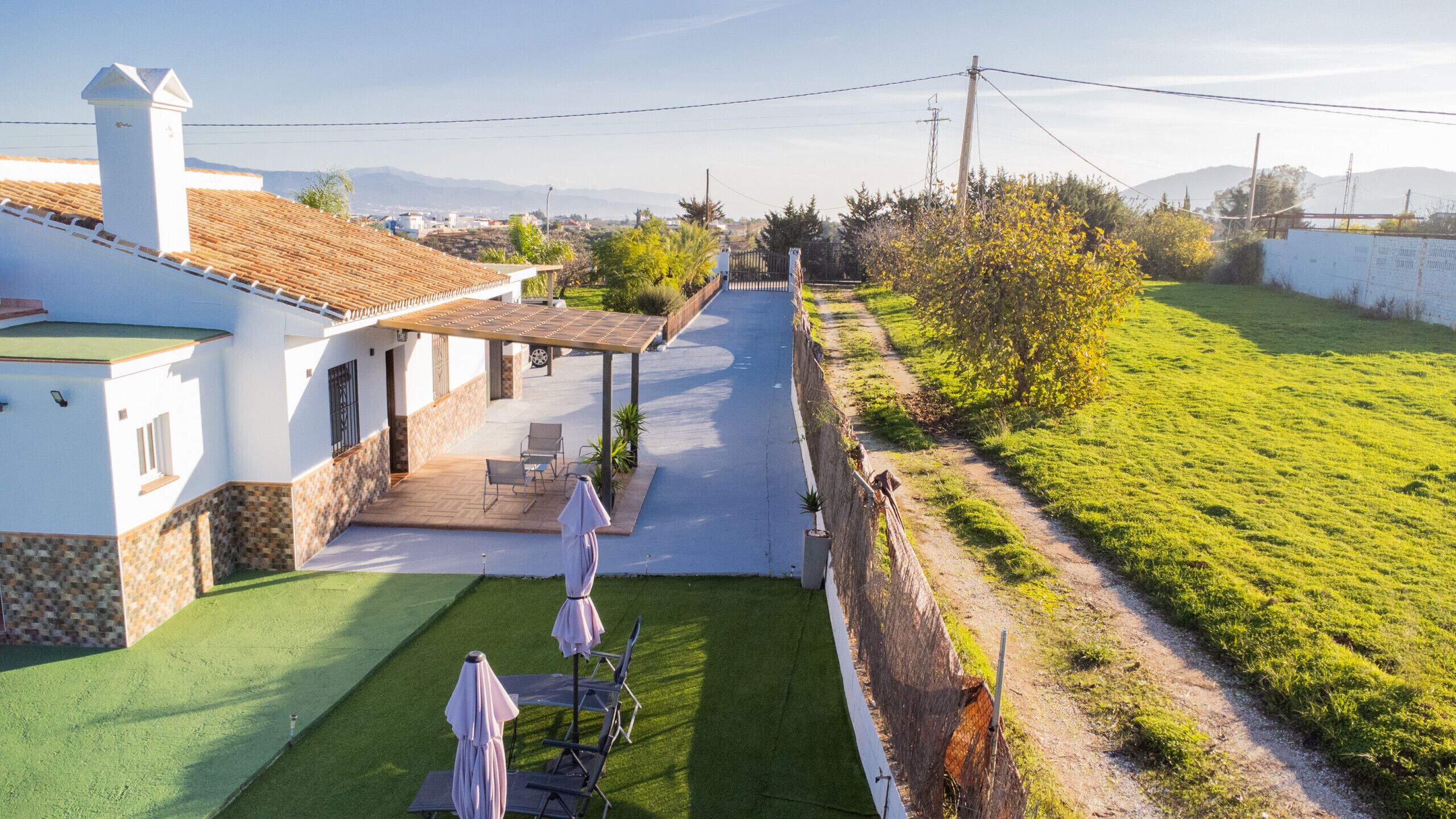 Ein Wohnhaus mit Terrasse, Sitzgelegenheit im Freien und Blick auf ein grünes Feld sowie ferne Berge.