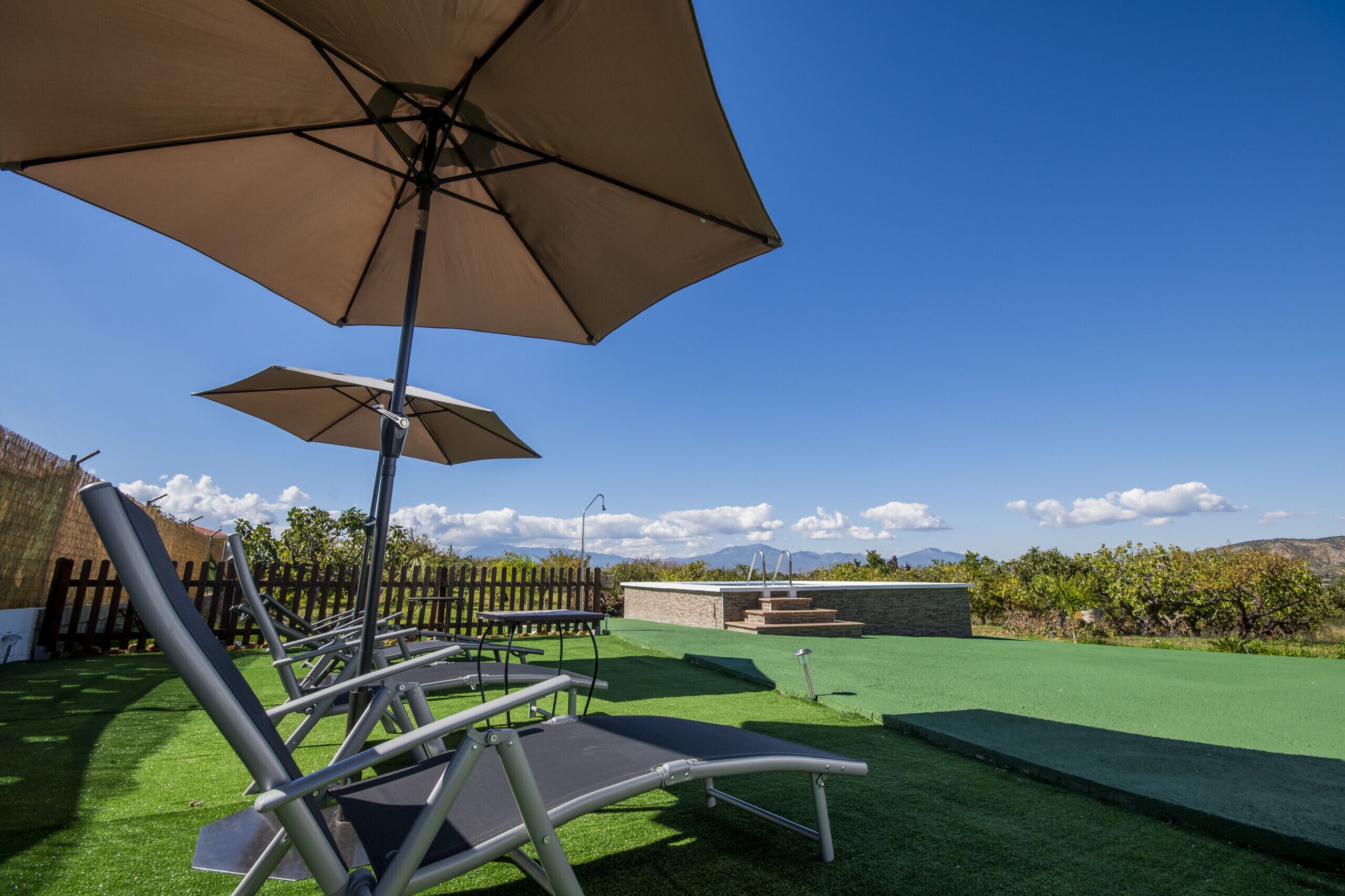 Een patio met twee lounge fauteuils, een grote parasol, een stenen bankje en een kleine tafel.