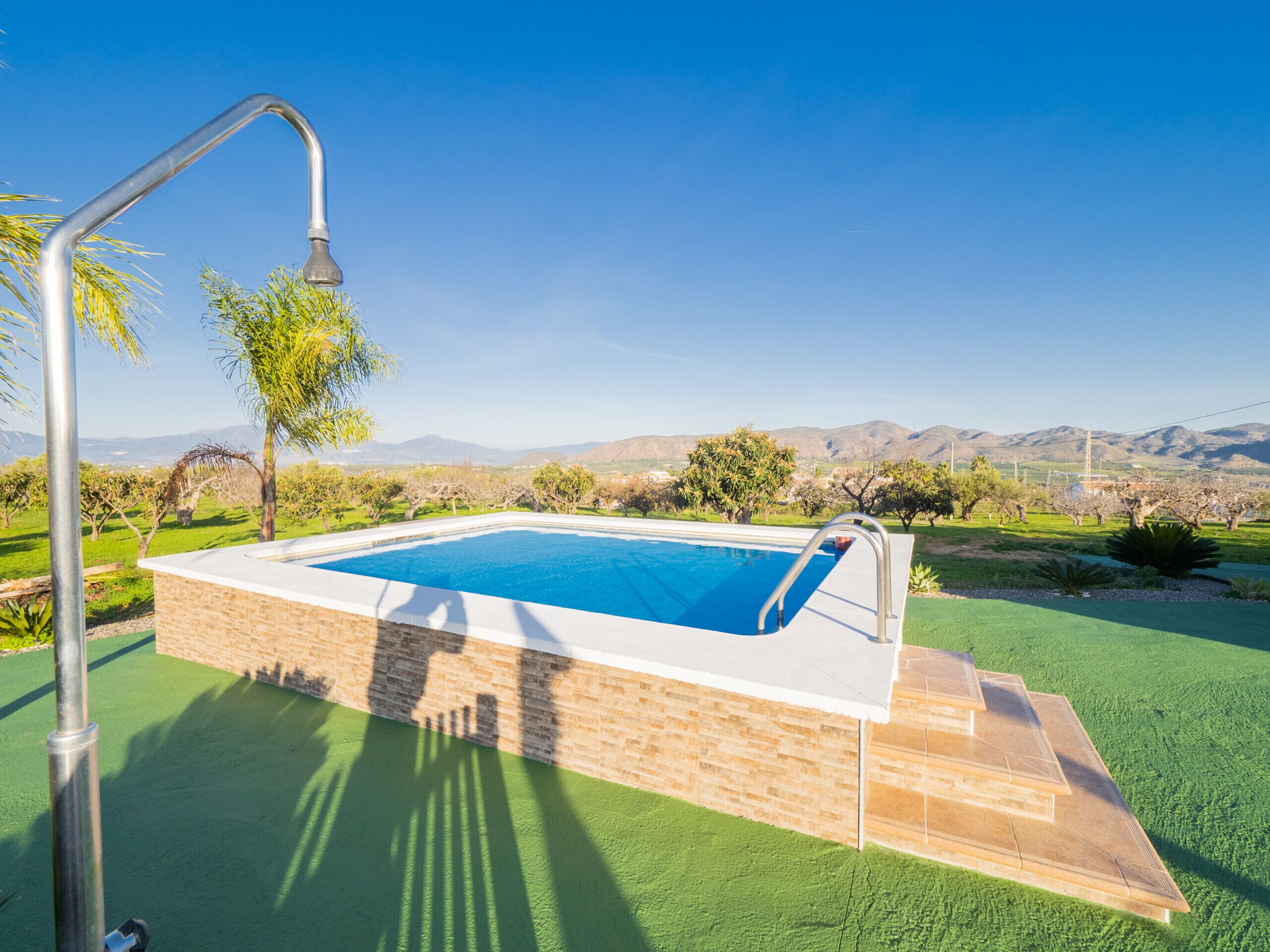 A rectangular swimming pool with a metal ladder on one side, surrounded by a brick wall and green artificial turf.