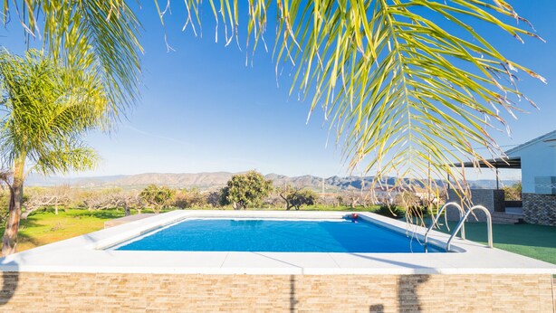 Una piscina rectangular con un muro de ladrillo y un cielo azul despejado al fondo.