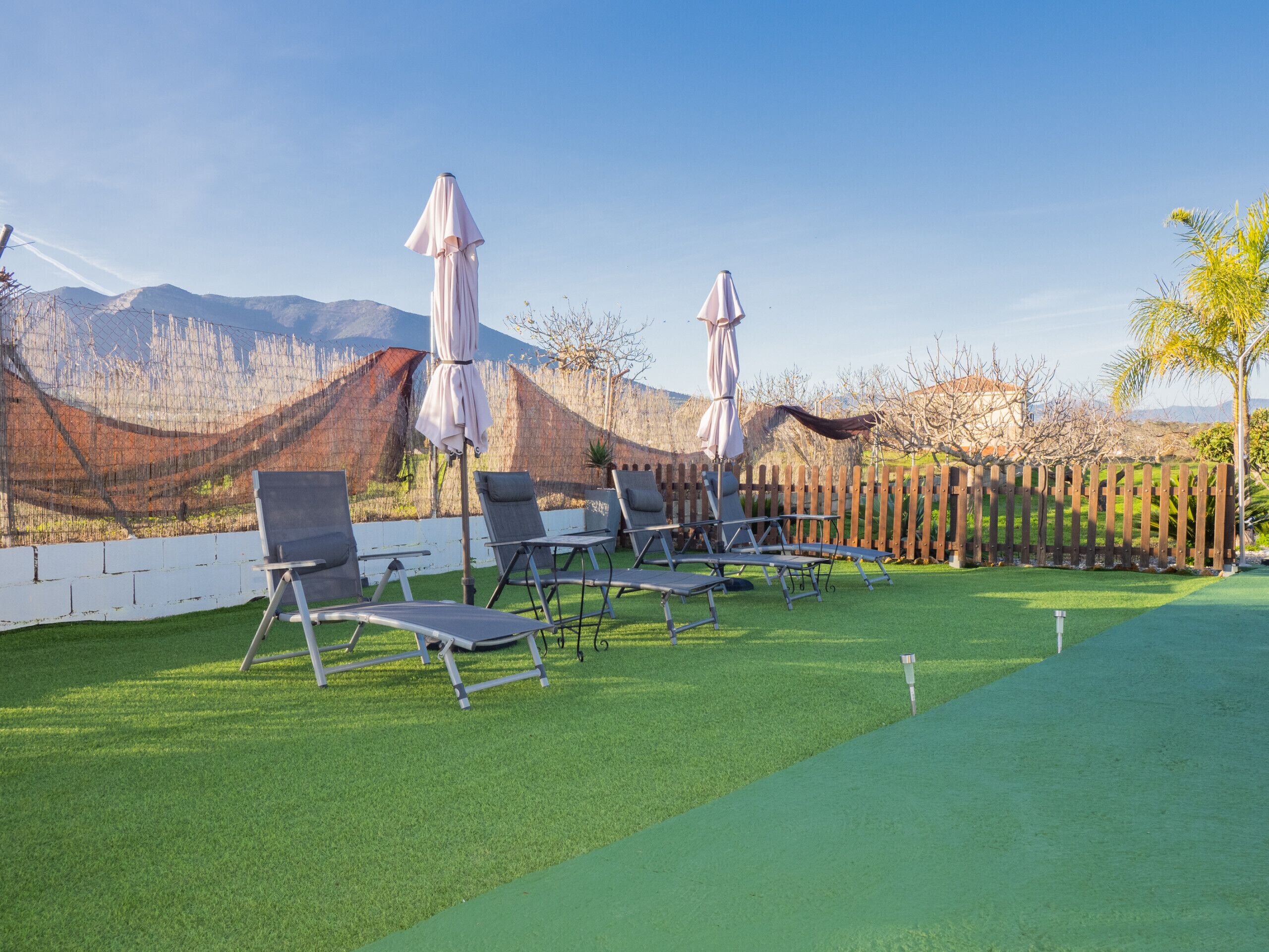 A pool area with lounge chairs and umbrellas, surrounded by a wooden fence and a view of mountains.