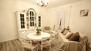 A cozy living room with a round dining table, white chairs, a beige sofa, and a white cabinet with glass doors. - SHABBY HOUSE GRANDMA PEPPA (Campello Sul Clitunno)