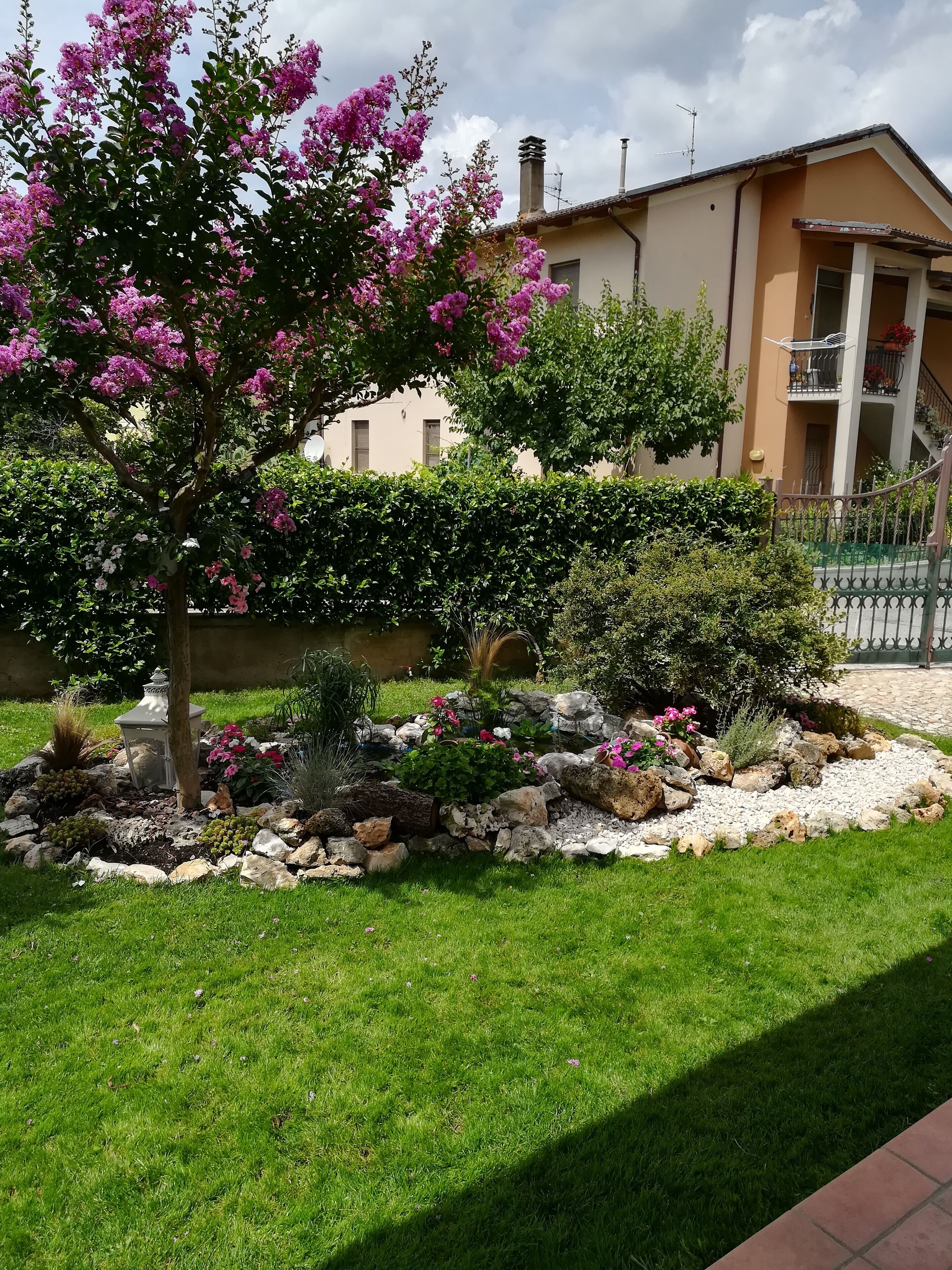 A well-maintained garden with a variety of plants and flowers, a stone pathway, and a building with a balcony in the background.