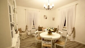 A dining room with a round table, white chairs, a chandelier, and a radiator. - SHABBY HOUSE GRANDMA PEPPA (Campello Sul Clitunno)