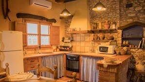 Een rustieke keuken met houten kasten, een stenen muur, een inbouwoven en een klein zithoekje met een tafel en stoelen.