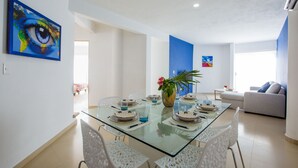 A modern dining area with a glass table, white chairs, and a blue accent wall. - Charming Huge PH with Private Rooftop and Jacuzzi (Playa Del Carmen)