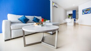 A modern living room with a grey sofa, blue cushions, a round coffee table, and a dining area with white chairs. - Charming Huge PH with Private Rooftop and Jacuzzi (Playa Del Carmen)