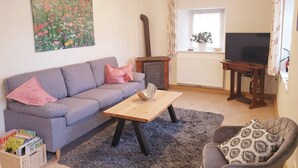 Una sala de estar con un sofá gris, una mesa de centro de madera, un sillón gris, un televisor y un cuadro en la pared.