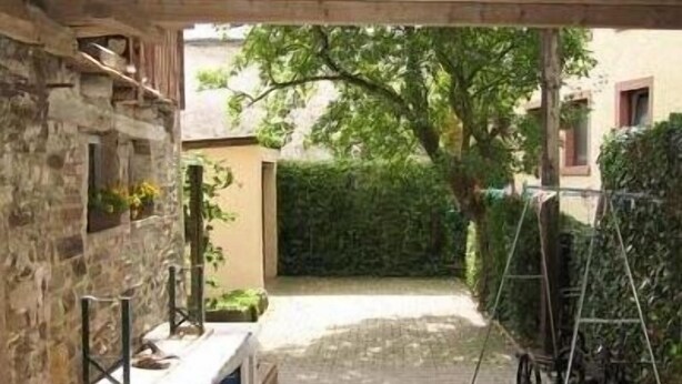 Un espacio al aire libre cubierto con una mesa y bancos de madera, paredes de piedra y un seto.