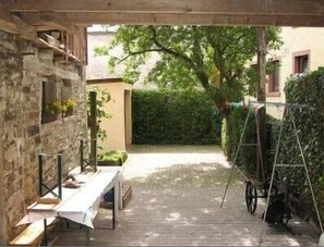 A covered outdoor area with a wooden table and benches, stone walls, and a hedge. - Former farm with a rebuilt barn and courtyard (Rheinland Pfalz)