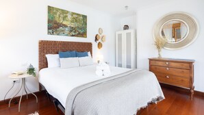A bedroom with a bed, a dresser, a nightstand, a painting, and a mirror.
