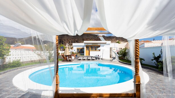 A swimming pool with a white deck, surrounded by a white fence, and a view of a mountain in the background.