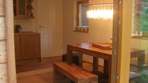 A wooden interior with a dining area, a kitchen, and a glass door leading outside.