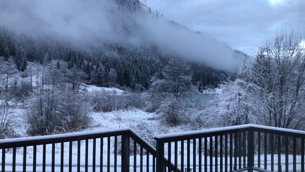 A snowy landscape with a mountain in the background and a wooden railing in the foreground.